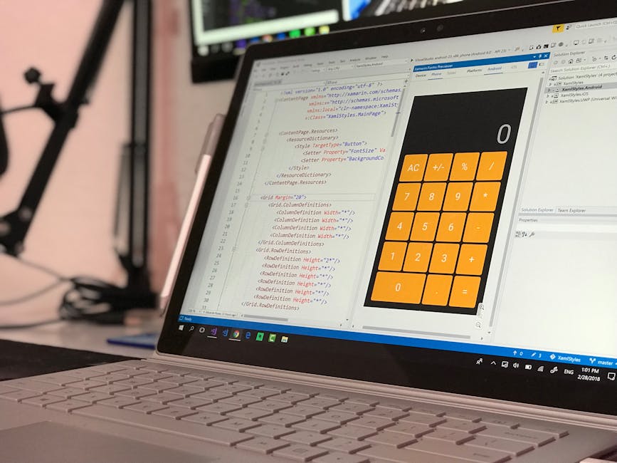 A close-up view of a sleek, modern laptop positioned on a desk, displaying a code editor on the screen alongside a large, bright calculator interface with orange buttons for digit inputs and basic ope